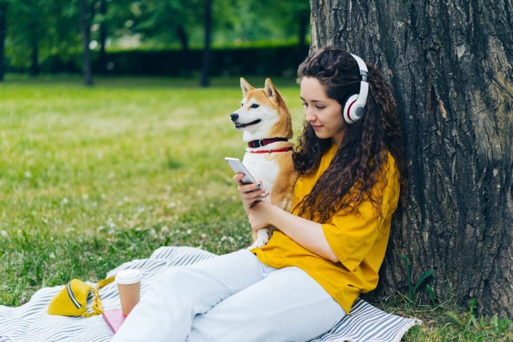pexels photo 20897113 about trackedtails A woman enjoys a relaxing day outdoors with her Shiba Inu, listening to music on headphones and using a smartphone.